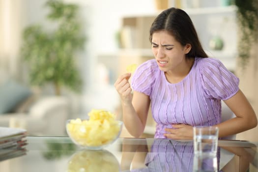 Woman suffering stomach ache eating chips at home
