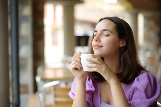 Woman relaxing smelling coffee aroma in a bar terrace