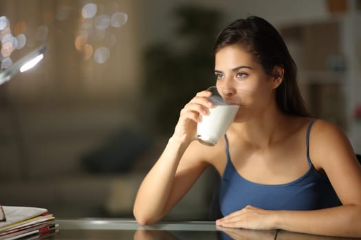 Woman in the night drinking milk at home looking away