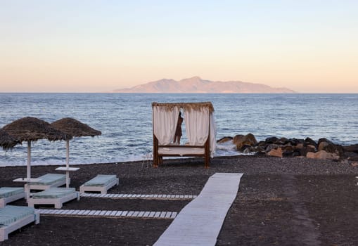 Sun loungers on the black volcanic beach of Kamari in Santorini. Cyclades, Greece