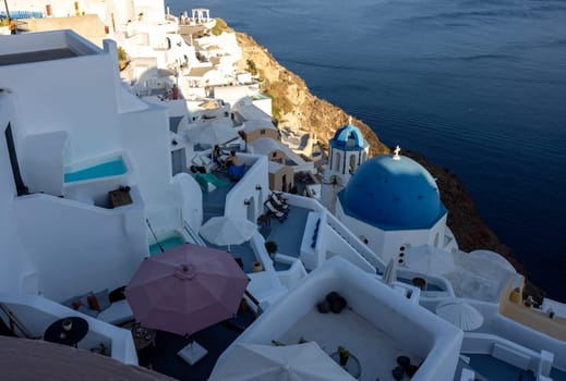 Oia, Santorini, Greece - June 28, 2021: View from viewpoint of Oia village with blue dome of  greek orthodox Christian church and traditional whitewashed greek architecture.  Santorini, Greece