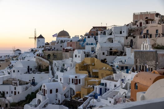 Oia, Santorini, Greece - June 28, 2021: Whitewashed houses and windmills in Oia in warm rays of sunset on Santorini island. Greece