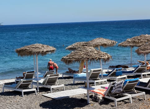 Kamari, Santorini, Greece - June 30, 2021: Sun loungers on the black volcanic beach of Kamari in Santorini. Cyclades, Greece