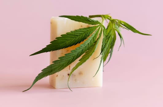 Craft soap bar near green cannabis sativa leaves on pink close up. Cosmetic Mockup, Copy space. Organic skincare beauty product. Eco friendly CBD soap