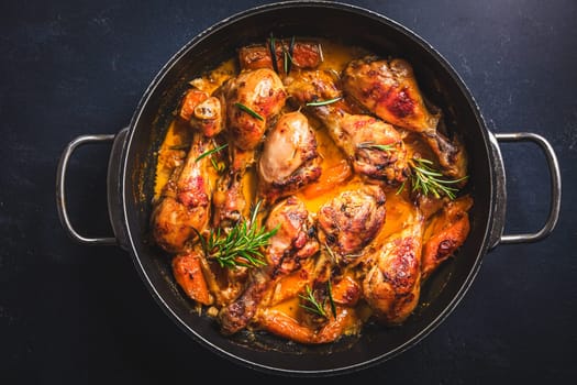 Baked chicken drumsticks with vegetables, casserole dish on black background