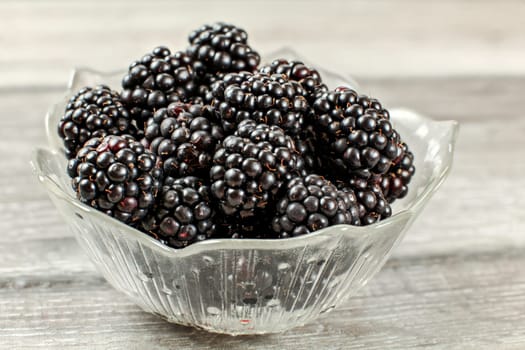 Detail photo - small glass bowl with blackberries on gray wood desk.