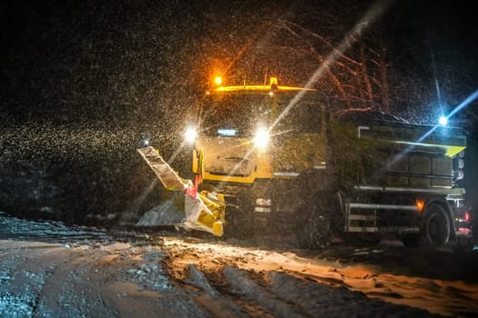 Highway maintenance truck cleaning road during heavy snowstorm in night, dangerous driving during winter transport calamity.