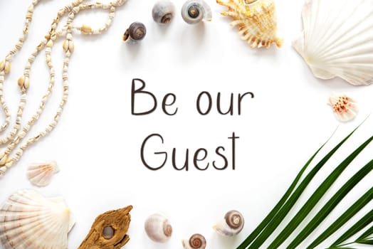 White Summer Flat Lay, Top View, Decorated With Shells and Plants, With English Text Be Our Guest