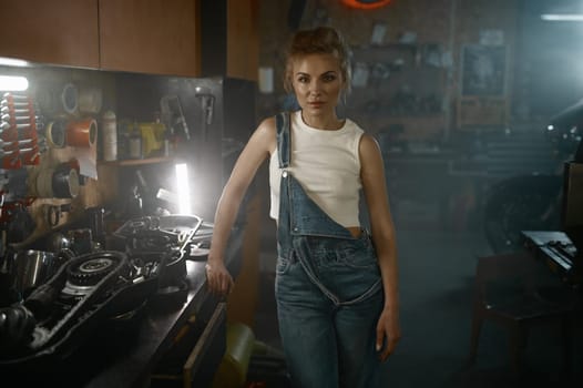 Portrait of young woman mechanic standing at workbench in motorcycle workshop