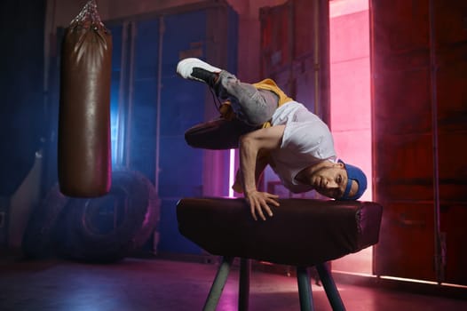 Young guy hiphop performer break dancing in neon club lighting. Male dancer bboying
