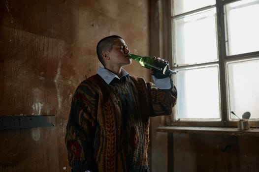 Lonely teenager girl drinking beer having alcohol addiction standing in abandoned shelter room