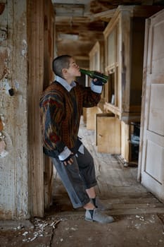 Homeless woman drinking beer from bottle living in abandoned house. Begging and alcohol addiction concept
