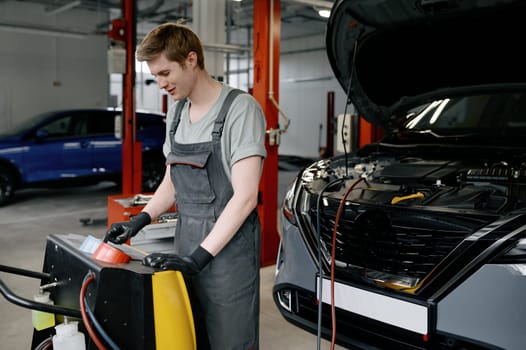 Man auto mechanic entering data on operation panel of automatic station for refilling of car air conditioner