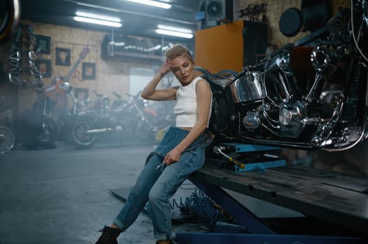 Attractive woman mechanic posing for camera at motorcycle garage. Professional repair woman at authentic workshop