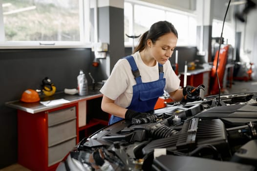 Young female tradesperson mechanic working on car engine using professional tools in auto repair garage