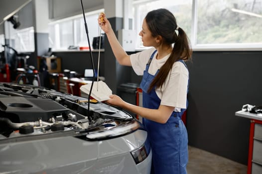 Young woman technician checking oil level in engine using dipstick in car mechanical workshop
