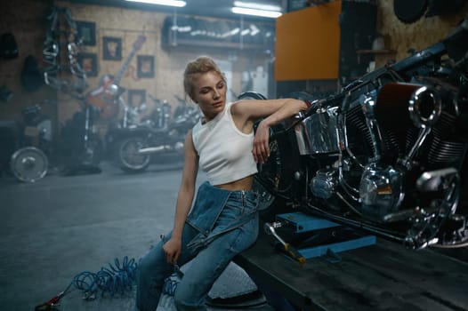 Attractive woman mechanic posing for camera at motorcycle garage. Professional repair woman at authentic workshop
