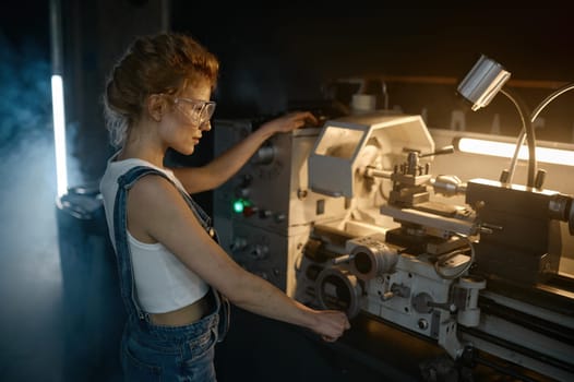 Young blond woman mechanical engineer working on manual lathe machine at motorcycle garage
