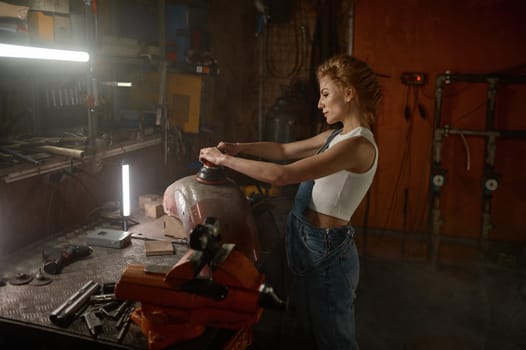 Attractive woman doing hard job at motorcycle garage using grinder to repair some metal bike part