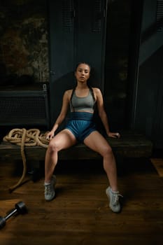 Tired exhausted woman boxer sitting on bench in gym. Young sportive girl resting after hard training