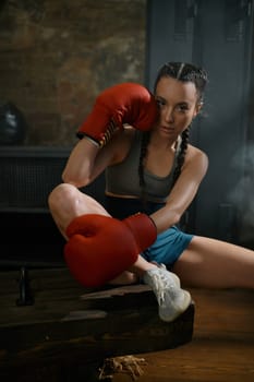 Young attractive woman boxer or kickboxer wearing tracksuit and punching gloves in loft gym. Martial arts and female concept