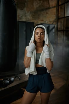 Close-up portrait of young woman boxer wearing kickboxing bandage on hands wrapped in towel feeling tired after training. Sport, fitness, lifestyle and people concept
