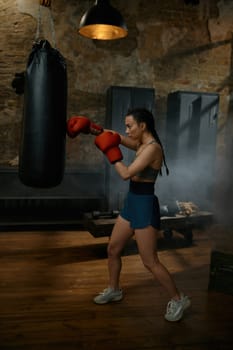 Strong girl fighter boxing with punching bag having workout training. Woman exercising self defense practice at gym
