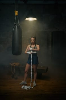Strong woman athlete wrapping her hands with boxing bandages. Female boxer preparing for practicing fighting exercise and kickboxing