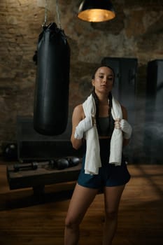 Satisfied woman boxer with towel on shoulders looking at camera. Sport, hobby and personal achievement concept