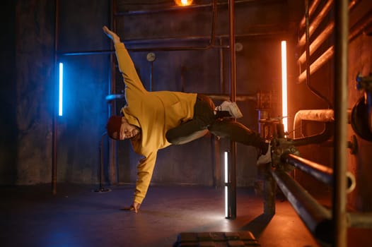 Modern hip hop dancer frozen in movie standing on one hand holding steel pilon tube practicing in dance over urban subway station background