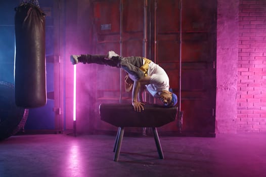 Male hip hop dancer on head stand doing acrobatic stunt using sports gymnastic apparatus. Hipster acrobat breakdancer