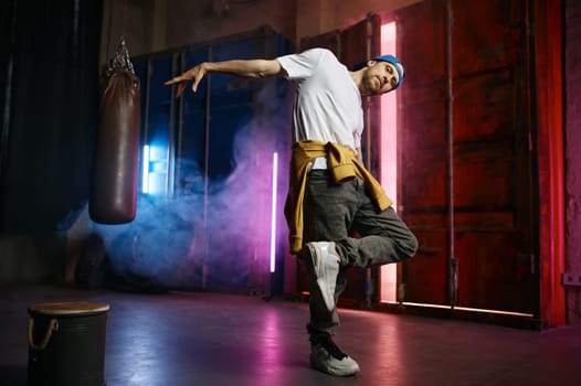 Cool and happy hip hop street dancer in trendy clothes dancing over loft studio background. Breakdancing concept