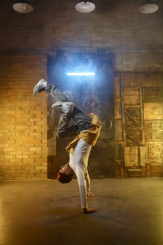 Handsome young man developing freeze over dance studio background in smoke and neon light. Breakdance freestyle performance concept