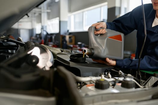 Closeup of mechanic pouring fresh oil into car engine from plastic container. Automobile maintenance and repair service station