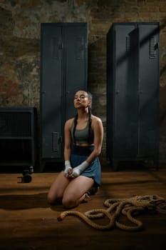 Beautiful woman boxer or kickboxer relaxing meditating sitting on floor in gym. Rest, sport, fitness and training concept