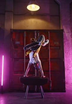 Sporty man breakdancer making acrobatic stunt balancing on hands in neon studio light