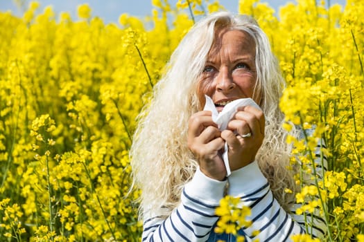 Woman suffers from allergy in a rape field and has to sneeze.