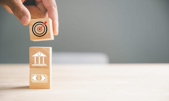 Wood block stacking guided by a hand symbolizes a strategic business plan and Action plan, focusing on the target. It represents business development and emphasizes growth and success.