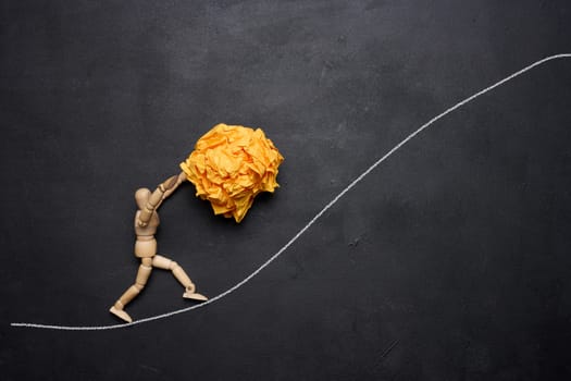 A wooden figurine of a person rolling a crumpled paper ball upwards, concept of perseverance and hard work, achieving goals.