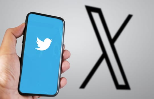 San Francisco, US, July 23 2023: hand holding a mobile phone with the Twitter X application on the screen. The new X logo blurred in the background. Illustrative editorial
