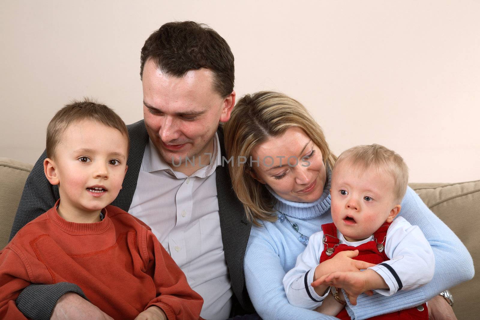 A family portrait of a mother and father sitting on a couch with their two young boys.  One boy has Down Syndrome.
