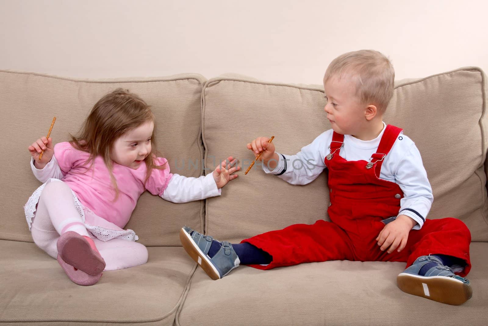 A little boy and girl with Down syndrome sitting on a sofa.