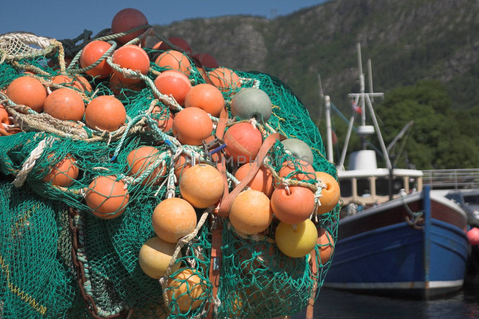 Fishing nets with bright orange floats in a dock; fishing boat in the background; background not in focus.