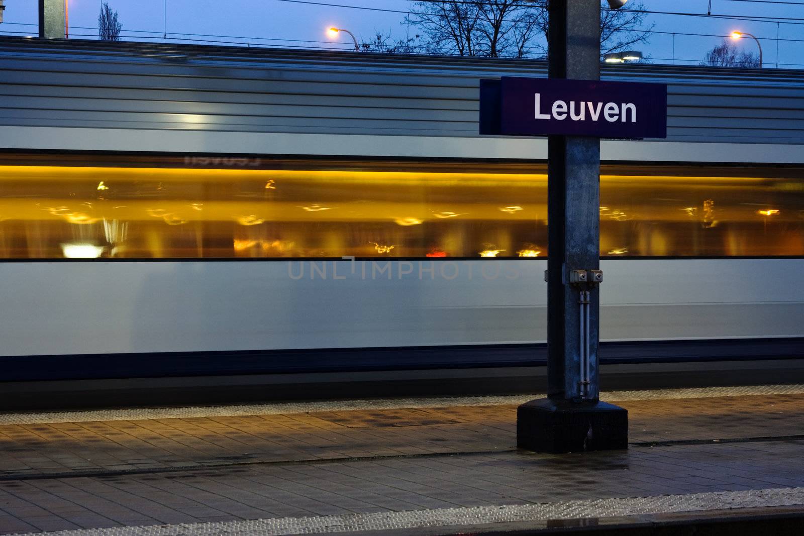 Train moving along platform in twilight (station Leuven)