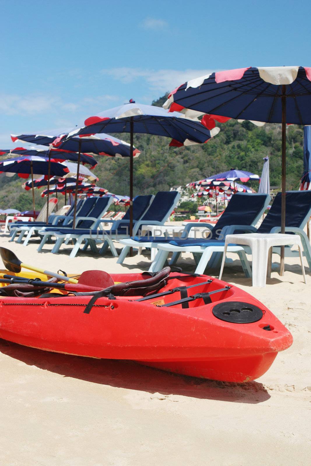 Red sea kayak on the beach surrounded by beach umbrellas.