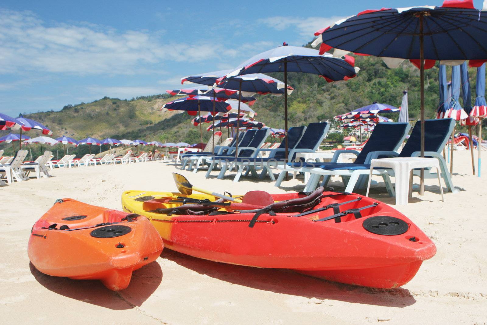 Two sea kayaks on the beach surrounded by beach umbrellas.