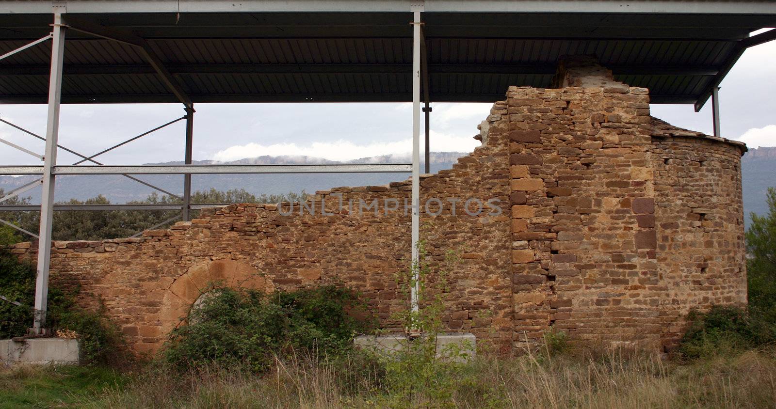 ruined chapel in Spain, sheltered by a metal roof, waiting for repair
