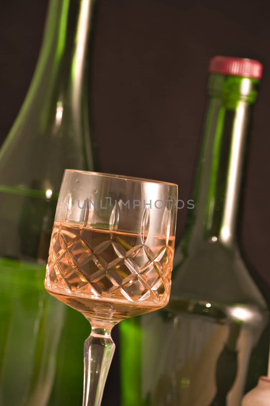 A cut glass containing whiskey or wine, with blurred bottles in the background