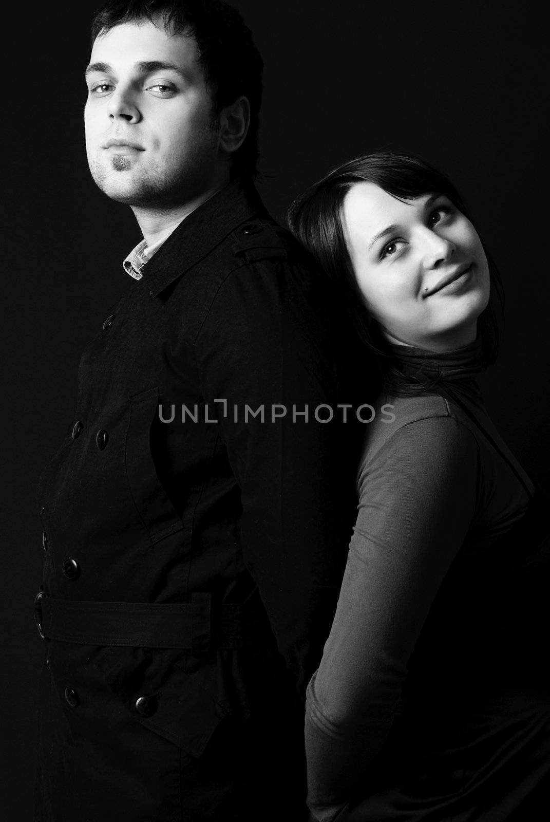 black and white studio portrait of a serious man and a dreamy young woman standing back to back
