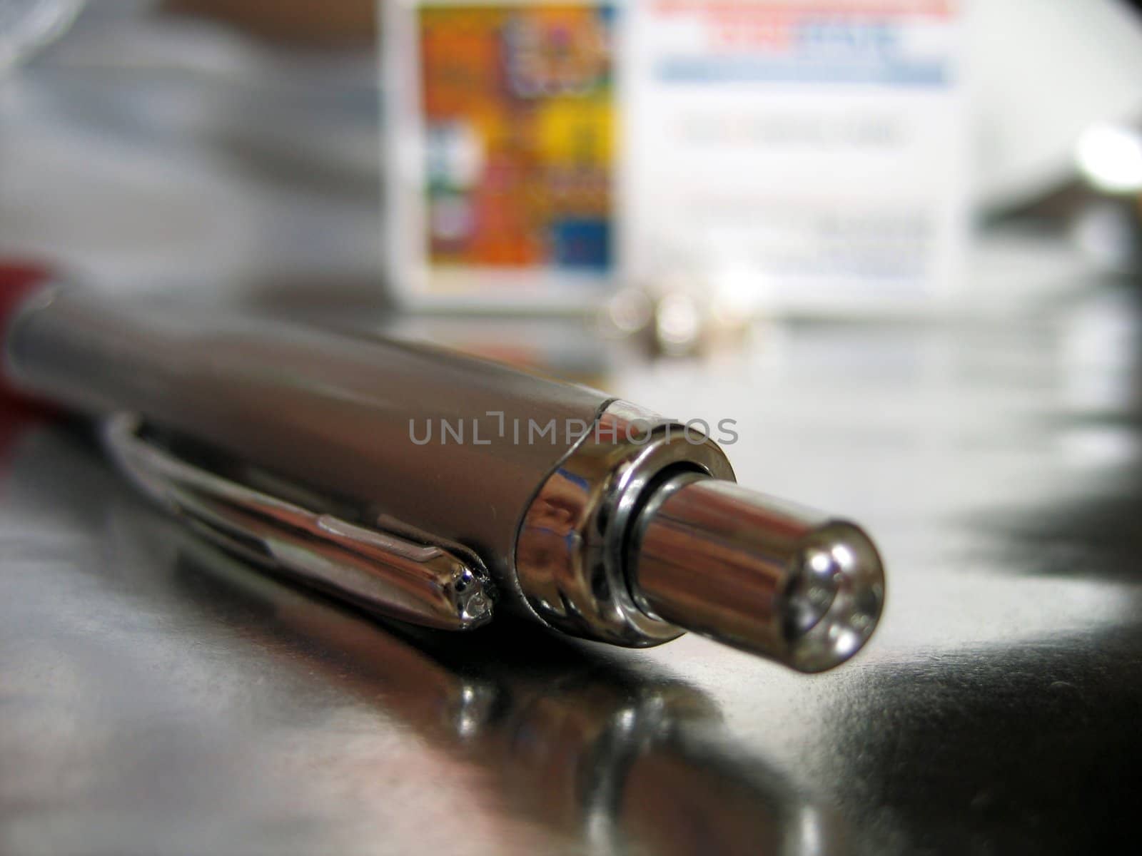 pen lying on a metalic surface with a visiting card in background